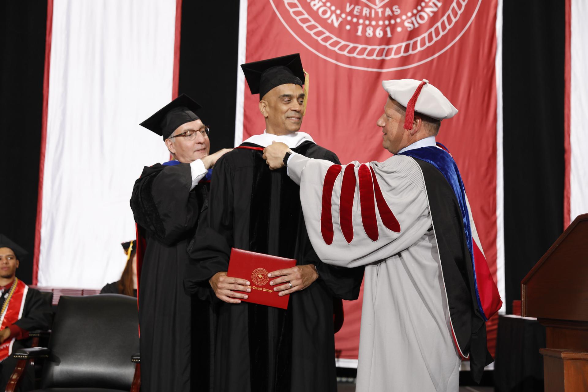 North Central College Commencement speaker Jim Williams is hooded by Board of Trustees Chair Jim McDermet and President Troy Hammond.