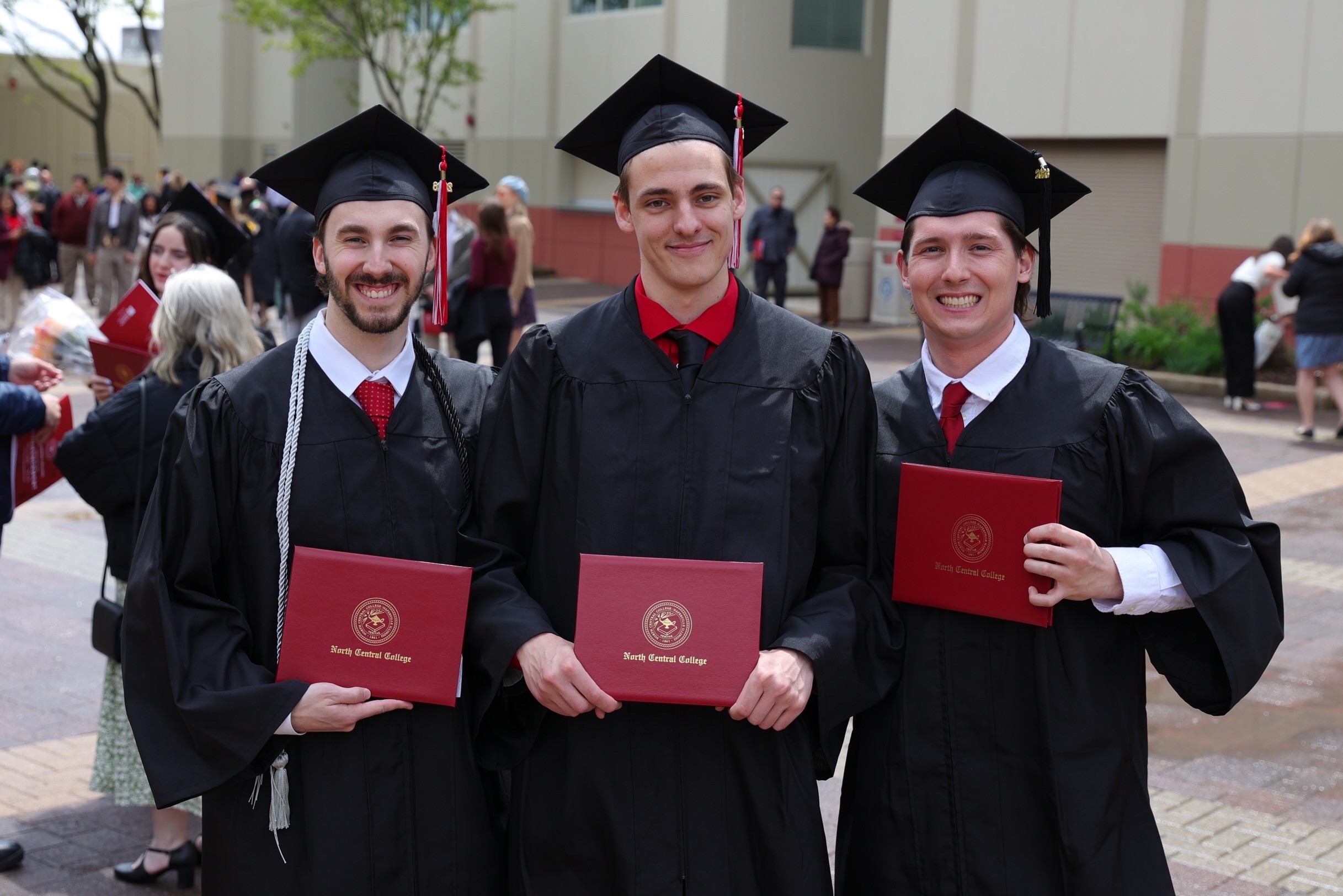 Three graduates are posing for a photo with their diplomas.