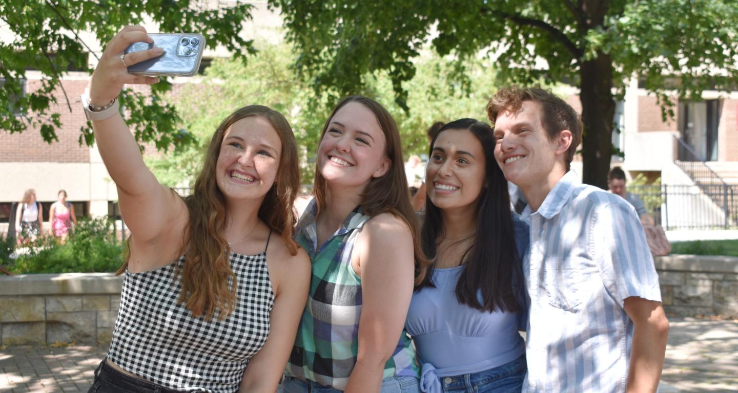 Four students are posing for a selfie outside on campus.