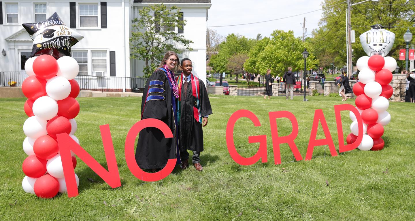 A professor and graduate are posing for a photo at Commencement.