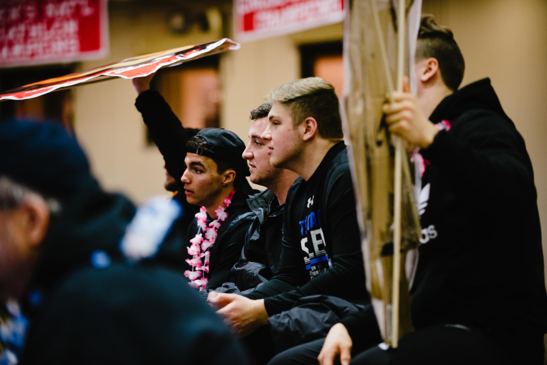 Student fans watching the North Central College men's volleyball game intently, holding up "fat head" posters made by the sport management class.