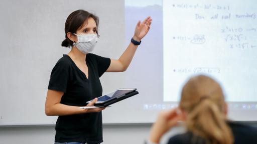 professor teaching with face mask on and a student (out of focus) in the bottom, right corner