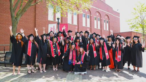 A group photo of graduates cheering with their hands in the air.