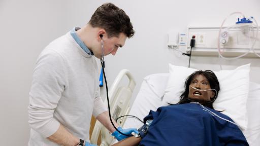 Student using stethoscope on mannequin patient in simulation lab 