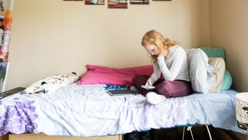 person sitting on dorm bed looking at laptop